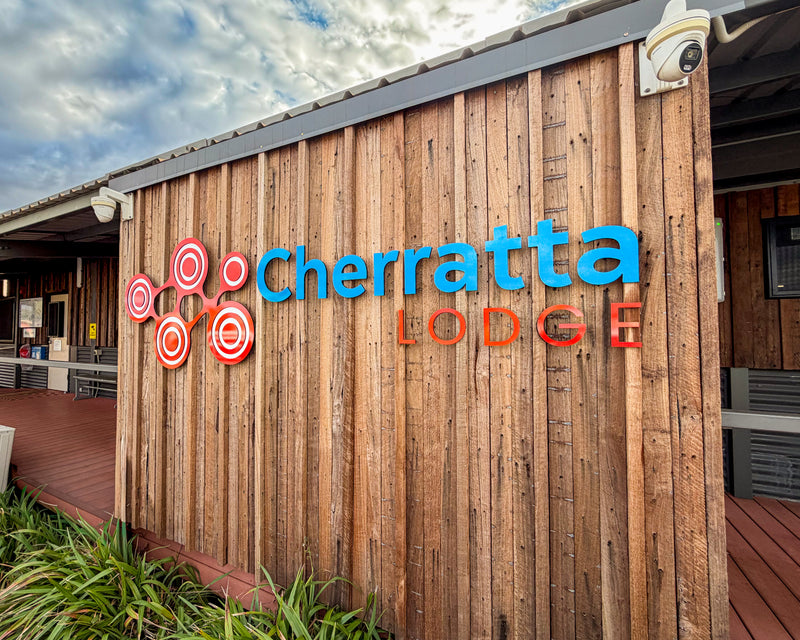 Cherratta Lodge custom fabricated signage mounted on a timber-clad exterior wall, featuring a red circular logo with blue and red dimensional lettering, installed by C Signs in Karratha.
