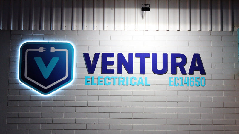 Ventura Electrical illuminated wall sign with blue logo and lettering mounted on a white brick wall, installed in Karratha by C Signs Pilbara.